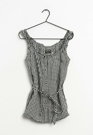Schwarz-weiß karierte ärmellose Bluse mit Rüschenkragen, Knopfleiste vorne und Taillenschleife, aufgehängt an einem schwarzen Kleiderbügel vor weißem Hintergrund.