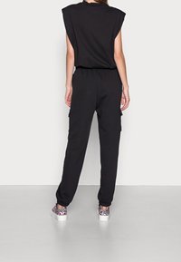 Svart jumpsuit med korta ärmar och elastisk midja, med sidofickor och smalnade ben. Bärs med mönstrade sneakers.