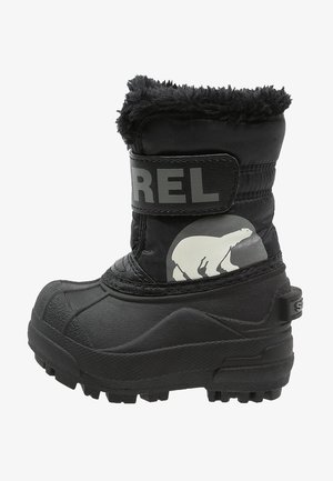 Botte d'hiver isolée noire avec semelle épaisse, doublure en fausse fourrure, sangle Velcro étiquetée "SOREL" et illustration d'ours polaire sur le côté.