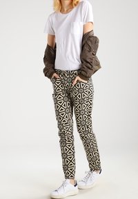 Slim-fit vzorované kalhoty s černobéžovým geometrickým designem, doplněné bílým tričkem a hnědým bomber jacketem. Bílé tenisky.