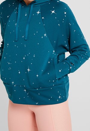 Turkis hættetrøje med hvide stjernemønstre, frontlomme og snore, båret sammen med lyserøde teksturerede leggings.