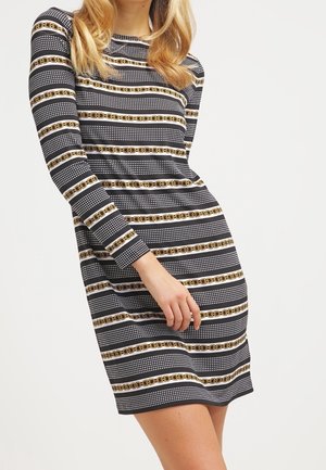 Robe à manches longues avec un motif rayé noir et blanc, ornée d'accents en chaîne dorée et de points texturés. Fabriquée dans un tissu lisse.