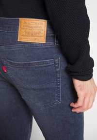 Mörkblå Levi's skinny taper jeans med en tan läderetikett på midjan, subtila sömdetaljer och en röd etikett på bakfickan.