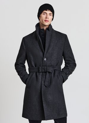 Dunkelgrauer Mantel aus Wollmischung mit hohem Kragen, Knopfverschluss und taillengürtel. Ergänzt wird der Look durch eine gerippte schwarze Mütze.