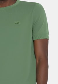 Camicia verde a maniche corte realizzata in tessuto liscio, con polsini a costine e un logo ricamato discreto sul petto.