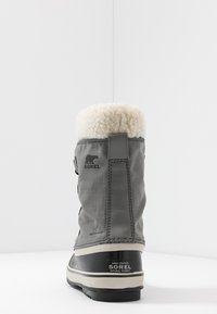 Botte d'hiver grise imperméable avec un dessus texturé et un col en fausse fourrure. Offre une semelle en caoutchouc noir et la marque Sorel sur le côté.