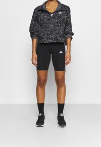 Svart leopardmönstrad pulloverjacka med zipkrage, i kombination med svarta åtsittande shorts med vita sidosträck och svarta sportskor.