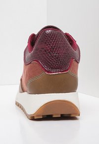 Chaussure de sport au design fusionné présentant une tige texturée bordeaux, un daim brun lisse, une semelle intermédiaire blanche et une semelle extérieure en caoutchouc avec traction.