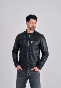 Černá kožená bunda se zipem vpředu, bočními kapsami a lehkou texturou. Má stojací límec a elegantní, přiléhavý střih.