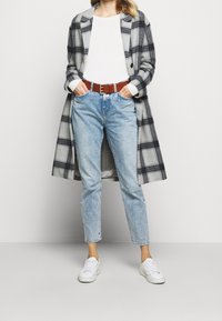 Grau-schwarzer karierter Wollmantel, weißes langärmliges Hemd, hellblaue Jeans, brauer Ledergürtel und weiße Sneakers.