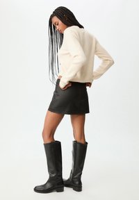 Maglione a maglia crema, mini gonna in denim nero e stivali alti fino al ginocchio in pelle nera con punta rotonda e tacco a blocco.
