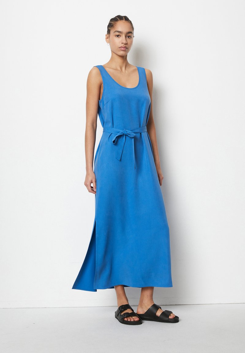 Blaues ärmelloses Maxikleid mit tailliertem Bund, seitlichem Schlitz und glatter Stofftextur. Trägt man mit schwarzen Sandalen. Schlichtes Design.