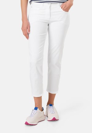 Weiße, taillierte Cropped-Hosen mit Slim Fit, ausgestattet mit Fronttaschen und einem Knopfverschluss. Kombiniert mit hellen Sneakers mit rosa Akzenten und blauen Details.