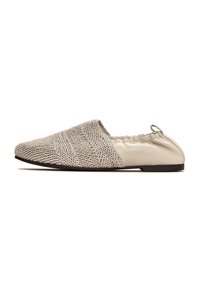 Parte superior de tejido beige con suaves acentos de cuero crema, apertura elástica suave y suela baja marrón, diseñado como un zapato tipo slip-on.