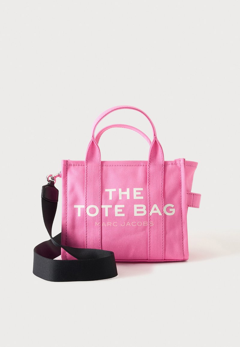 Sac fourre-tout en toile rose avec deux anses et une bandoulière noire réglable, texte « THE TOTE BAG MARC JACOBS » sur le devant.