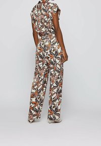El mono con estampado floral presenta un diseño de manga corta, pierna ancha y cintura ceñida con cinturón. Los colores incluyen beige, negro, naranja y rosa. Tejido suave.