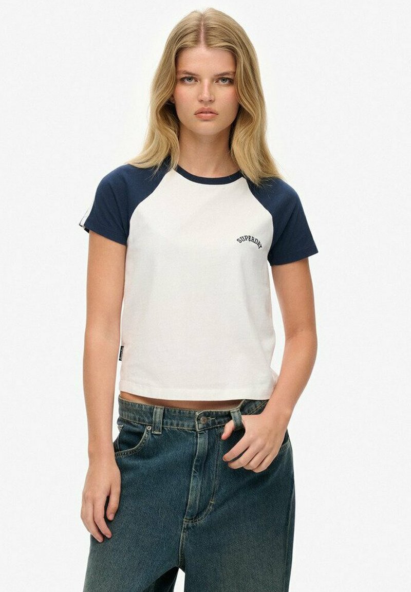 Camiseta recortada con cuerpo blanco y mangas raglán azul marino; presenta el logo de "Superdry" en el pecho; fabricada en una suave mezcla de algodón.