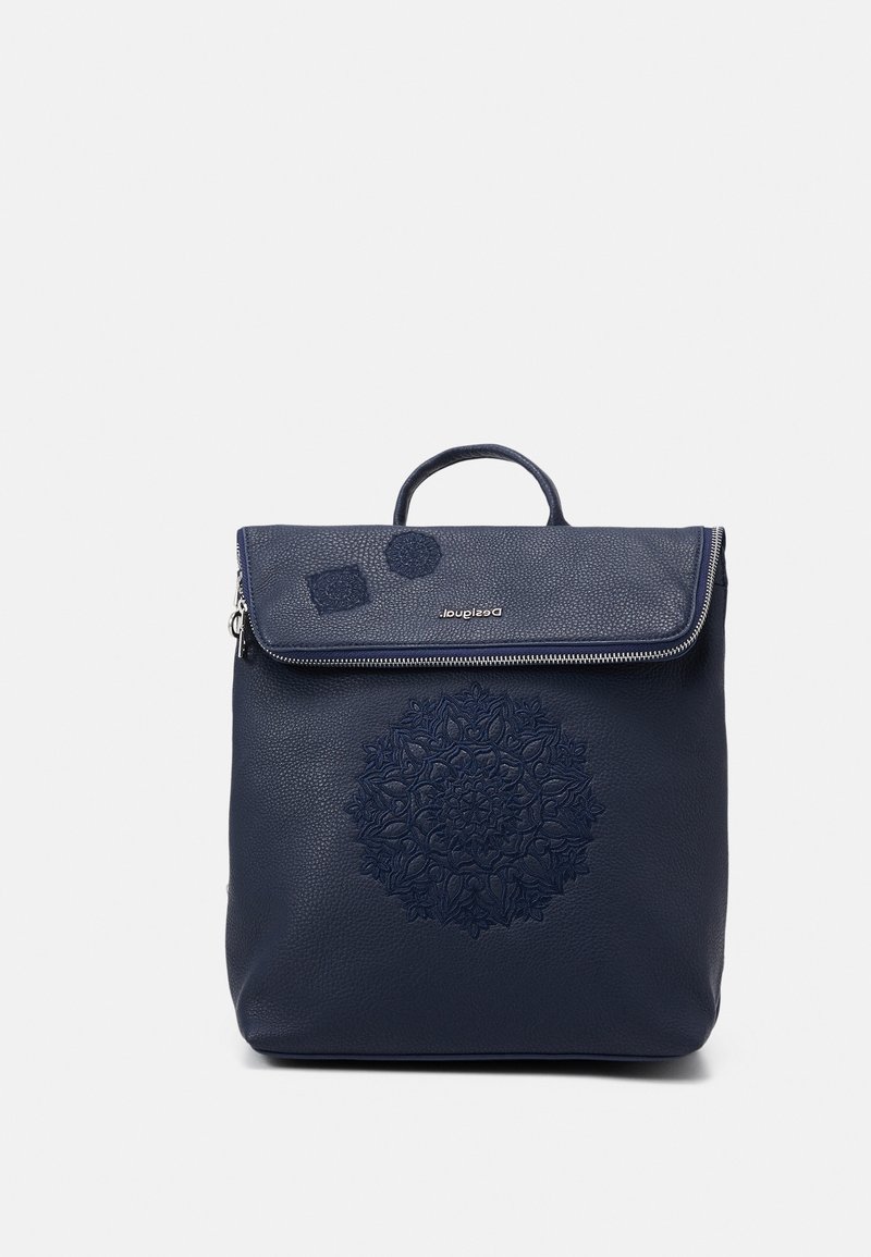 Sac à dos en cuir bleu marine avec rabat zippé pliant, poignée supérieure et motif floral circulaire embossé à l'avant.