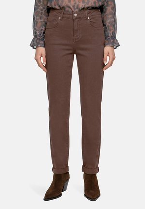 Kvinde iført brune jeans med lige ben og opsmøgede kanter samt mørkebrune ruskindssko til anklen, kombineret med en gennemsigtig bluse med dyreprint.