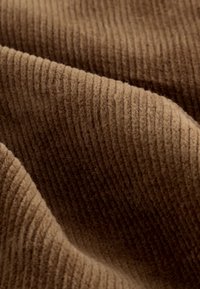 Tissu en velours côtelé marron présentant de fines côtes verticales et une surface douce et texturée, mettant en valeur la chaleur et la profondeur de la couleur.