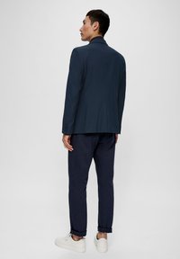 Marineblaues maßgeschneidertes Sakko mit Revers, kombiniert mit dunklen Hosen und weißen Sneakers; glattes Material mit dezenten Mustern.