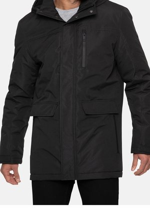 Homme portant un manteau d'hiver noir à capuche avec une poche zippée sur la poitrine et deux poches à rabat à l'avant, visible du cou jusqu'au milieu des cuisses.