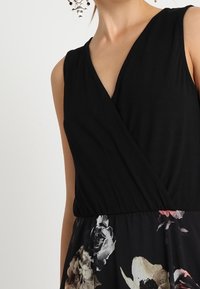 Robe noire à manches longues avec imprimé floral à la taille, en tissu doux, avec un corsage ajusté et de larges bretelles. Design élégant avec une texture subtile.