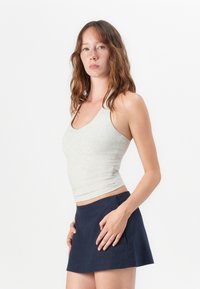 Grijze, aansluitende tanktop met een scoop halslijn en geribde structuur, gecombineerd met een marineblauwe, uitlopende minirok. Model poseert met één hand op de heup.