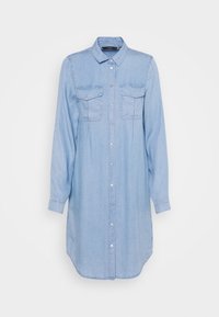 Ljusblå denimskjolk med knappstängning framtill, långa ärmar, två bröstfickor och rundad nederkant. Slät textur, avslappnad design.