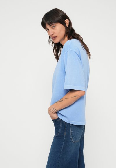 Ανοιχτό μπλε βαμβακερό μπλουζάκι με άνετη εφαρμογή, κοντά μανίκια και στρογγυλή λαιμόκοψη. Συνδυασμένο με σκούρο μπλε τζιν παντελόνια.
