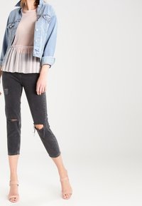 Džínová bunda, světle modrá; průhledná, růžová blůza s sklady; černé zkrácené džíny s roztrženými detaily; světle růžové lodičky.