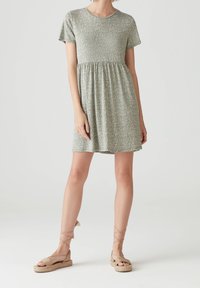 Robe à manches courtes de couleur vert clair avec un motif floral, taille cintrée et jupe fluide. Associée à des sandales espadrilles beiges.