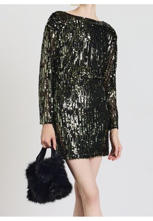 Femme portant une mini-robe à manches longues noire et dorée à sequins, tenant un petit sac à main noir en fourrure sur un fond uni.