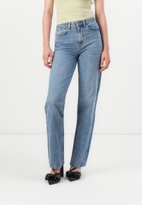 Lichtblauwe denim straight-leg jeans met een hoge taille, voorzien van zijzakken en een gladde textuur. Vergezeld door zwarte hakken.