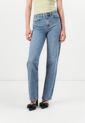 Jean droit en denim bleu clair à taille haute, avec des poches avant et une texture lisse. Accompagné de chaussures à talons noires.