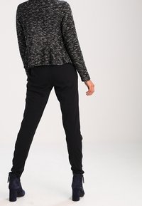 Pull texturé noir, coupe ample, associé à un pantalon noir fuselé. Le mannequin porte des bottines bleu marine avec des lanières à l'arrière.