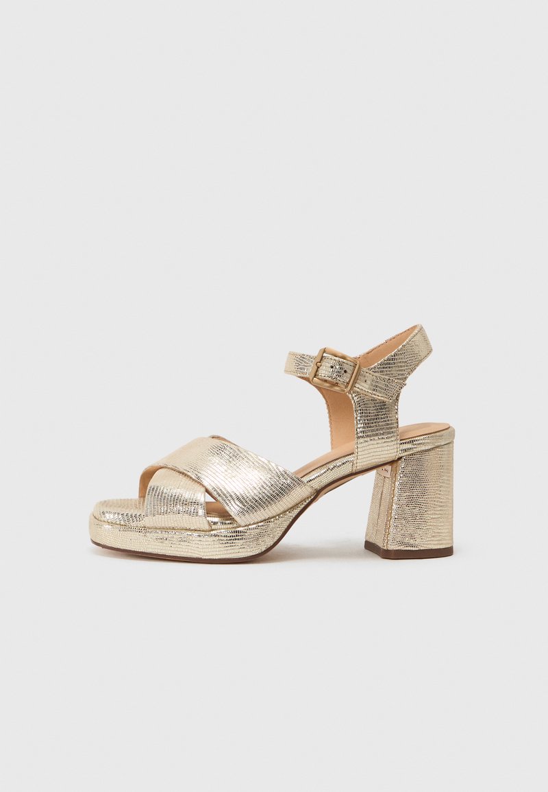 Guld metalliske hæle sandaler med en chunky blokhælkonstruktion, krydsremdesign og en ankelrem med spænde. Tekstureret overflade.