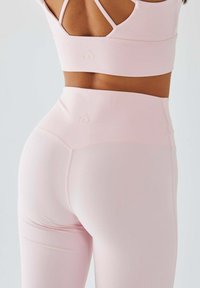 Jasnoróżowy zestaw sportowy składający się z dopasowanego stanika sportowego z logo w kształcie serca oraz legginsów z wysokim stanem wykonanych z gładkiego, elastycznego materiału.