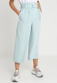 Light blue, high-waisted culottes with pleats and a belt featuring a silver buckle. Pair of white and gray sneakers with patterned laces.