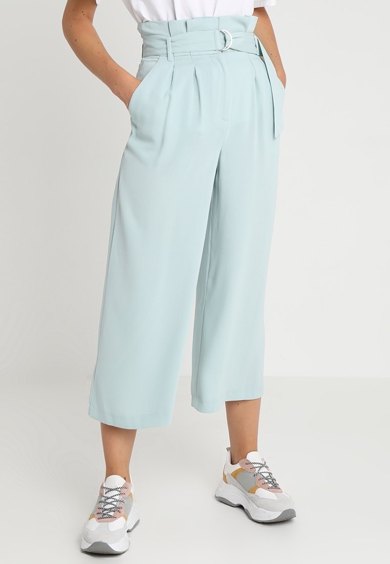 Light blue, high-waisted culottes with pleats and a belt featuring a silver buckle. Pair of white and gray sneakers with patterned laces.