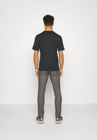 Svart kortärmad T-shirt, grå figurnära byxor och bruna och vita sneakers. Synlig sömnad och avslappnad passform vid axlarna.