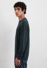 Dunkelgrüner Strickpullover mit Rundhalsausschnitt, langen Ärmeln und gerippten Bündchen und Saum. Glatte Textur, taillierte Silhouette.