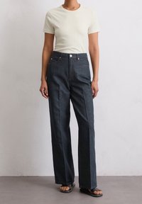 Vaaleanbeige vartalonmyötäinen t-paita yhdistetty tummansinisiin, leveälahkeisiin farkkuihin, joissa on korkea vyötärö, nappisuljenta ja kontrastivärinen ompelu.