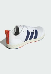 Biele tenisky s námorníckymi modrými pruhmi, textúrovanou gumovou podrážkou a oranžovou nášivkou na päte. Obsahujú suchý zips a polstrovaný golier.