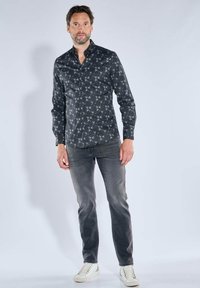 Schwarzes Hemd mit subtilem geometrischem Muster, Button-Down-Kragen, kombiniert mit grauen Jeans und weißen Sneakern. Glatter Stoff, maßgeschneiderte Passform.