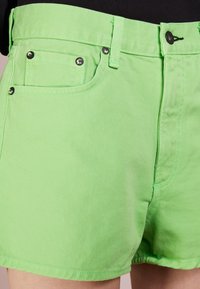 Des shorts en denim vert lime avec un design à cinq poches, une fermeture à bouton métallique et des détails de couture contrastants.