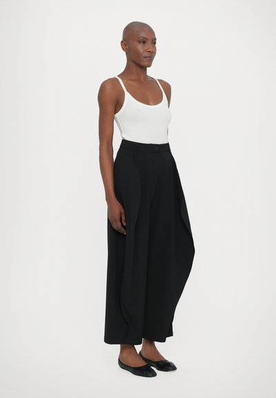 Black wide-leg trousers with a tailored fit, featuring a high waist, subtle pleats, and a matching button closure. Paired with a white tank top.