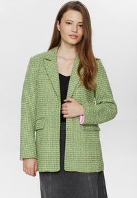 Grön tweed blazer med rutmönster, slagkrage och rosa detaljer vid ärmarna. Har två framfickor och en knappstängning.