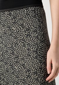 Robe noire avec un motif texturé de formes irrégulières beiges. Présente un corsage ajusté et une jupe fluide avec une taille élastique.