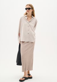 Light beige button-up shirt with a collar, paired with a ribbed, knee-length skirt in a matching shade. Black oversized sunglasses and sandals.